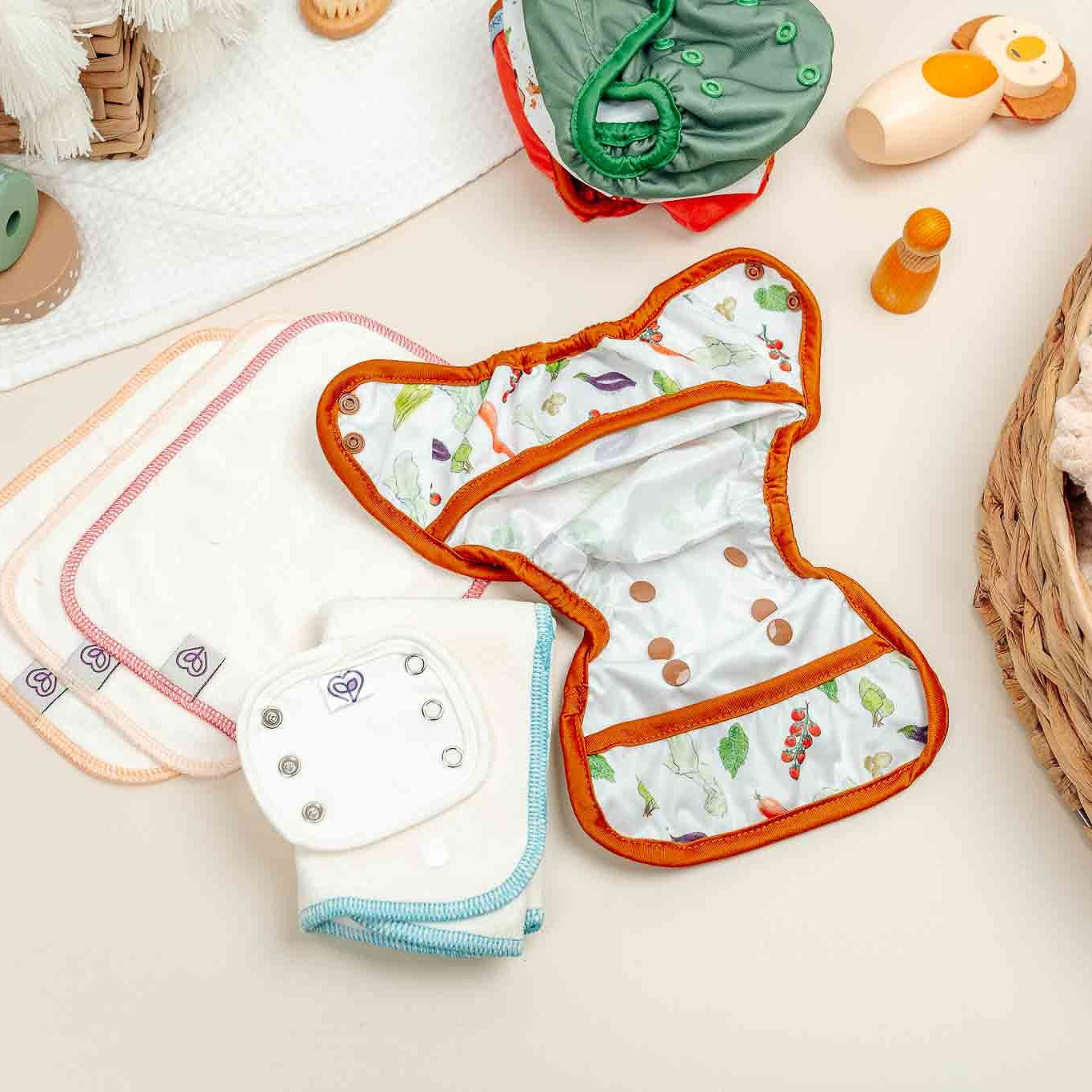Baby diapers with colorful patterns on a light surface with toys and a basket in the background.