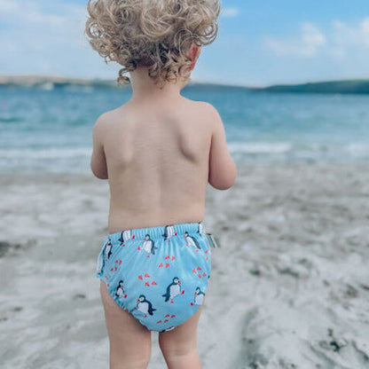 Child wearing a blue swim diaper with penguin design on a beach