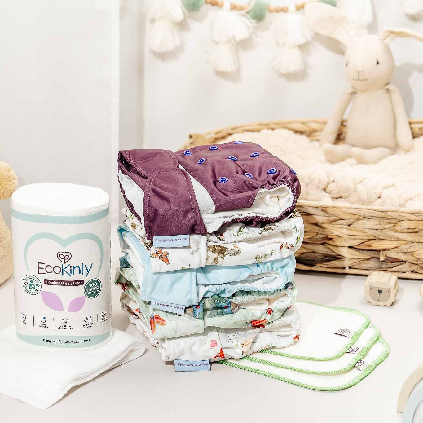 Stack of baby diapers with an EcoKindly container on a white surface, surrounded by baby toys and items.