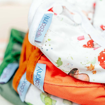 Stack of colorful baby clothes with 'EcoKini' labels on a blurred background